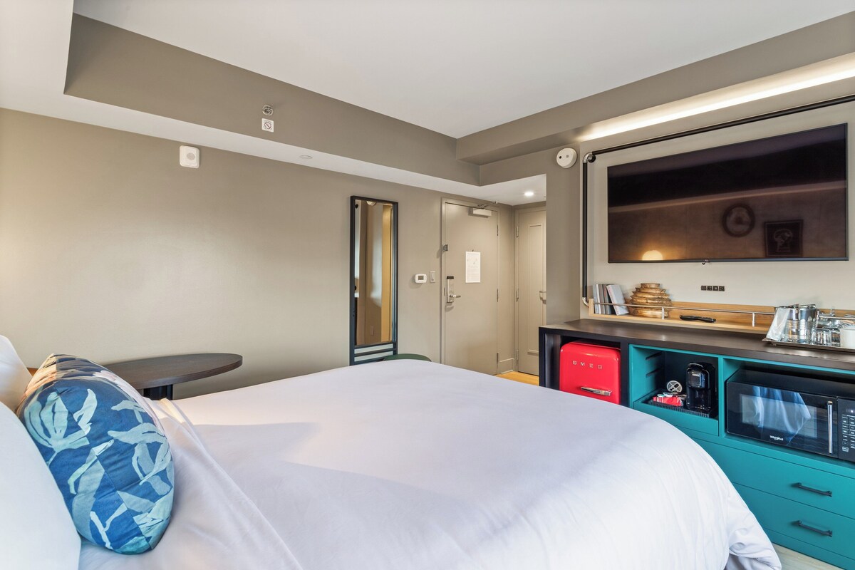 A hotel room with a bed, a desk, a microwave, and a TV.