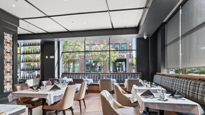 Restaurante com mesas, cadeiras, um banco e vista para um edifício com uma placa que diz 