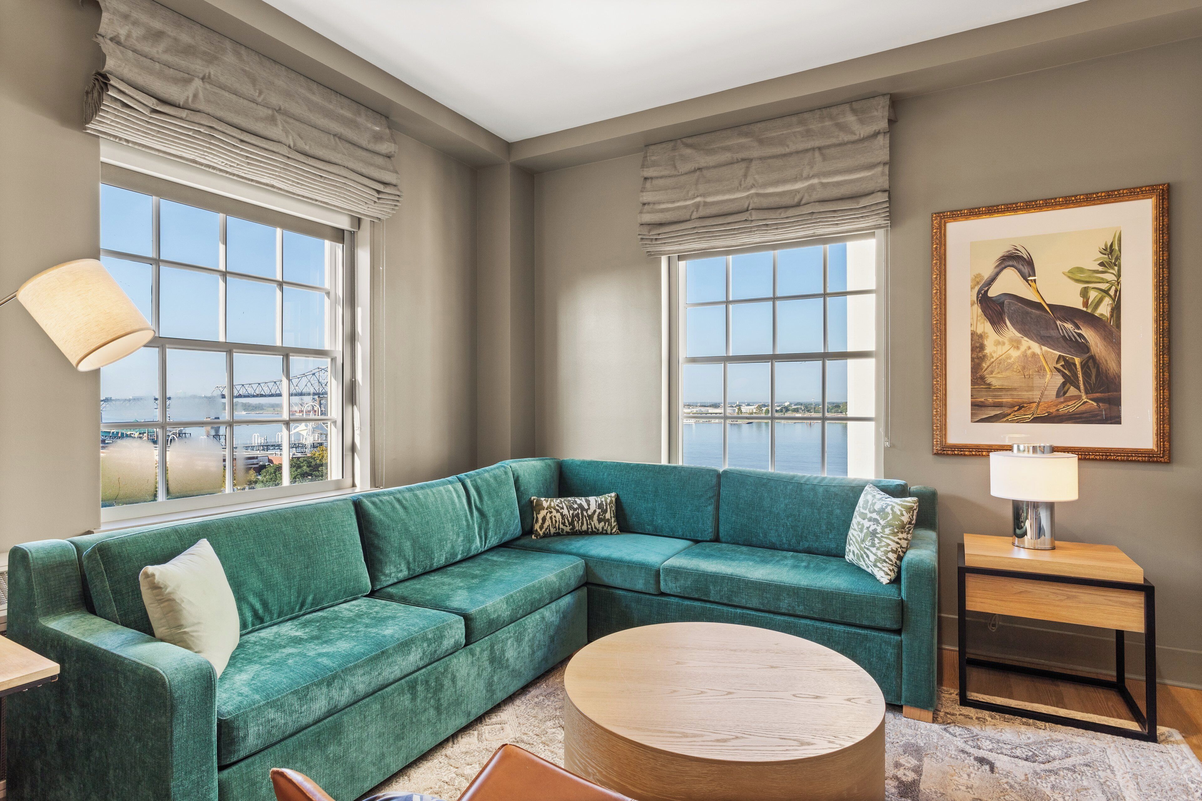 Sala de estar con un sofá seccional color turquesa, una mesa de centro redonda y vistas de la ciudad a través de ventanas amplias con cortinas.