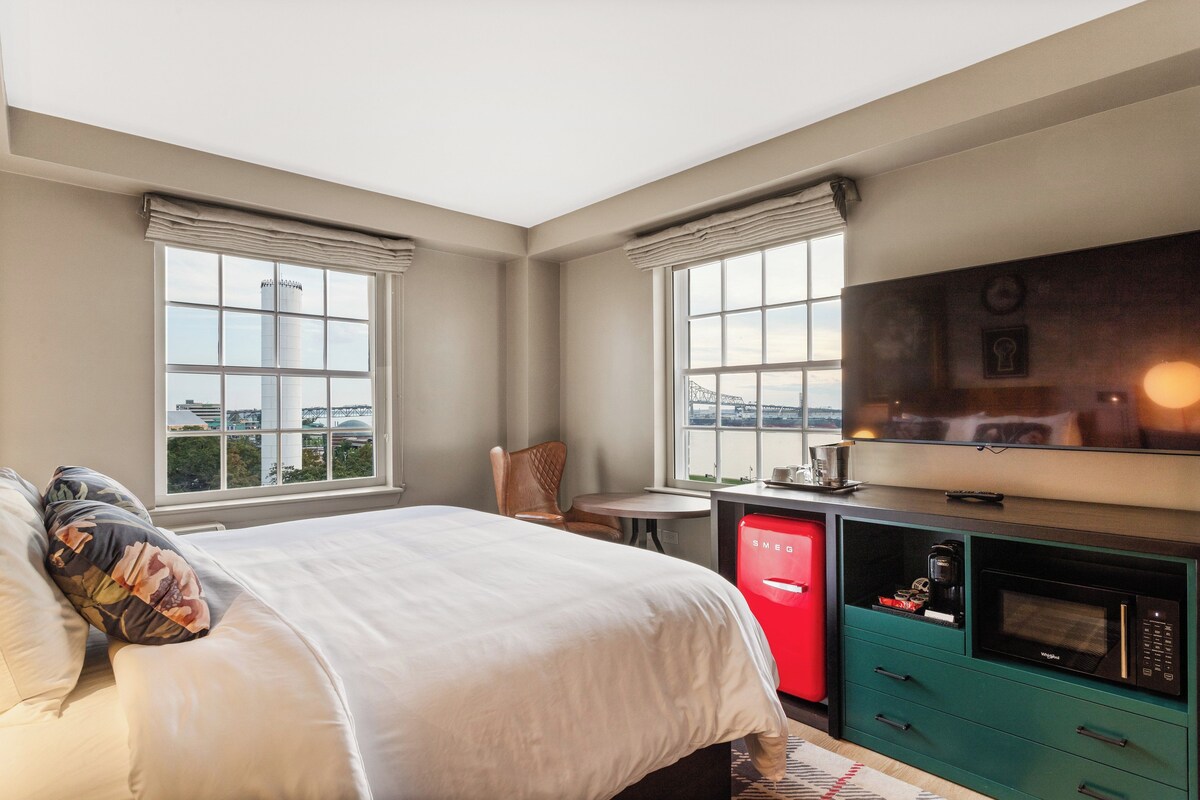 A hotel room with a bed, a TV, a red minibar, and a view of a cityscape.