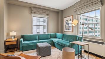 A modern living room with a teal sectional sofa, a small ottoman, a round coffee table, and a floor lamp.