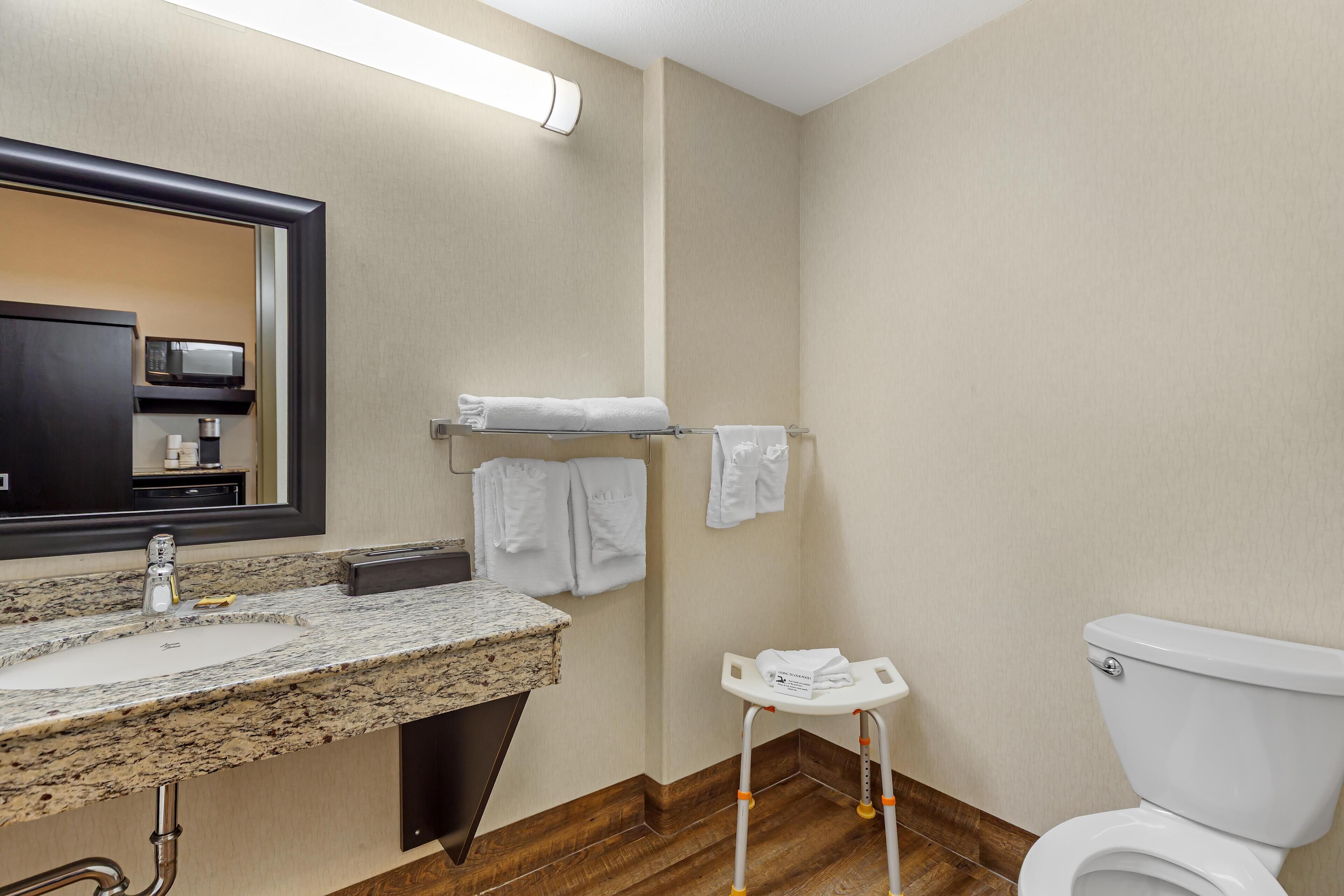 A bathroom with a granite countertop sink, a mirror, a towel rack, a white toilet, and a small step stool.