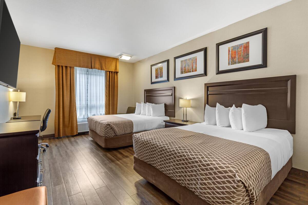 A hotel room with two beds, a desk, and a TV.