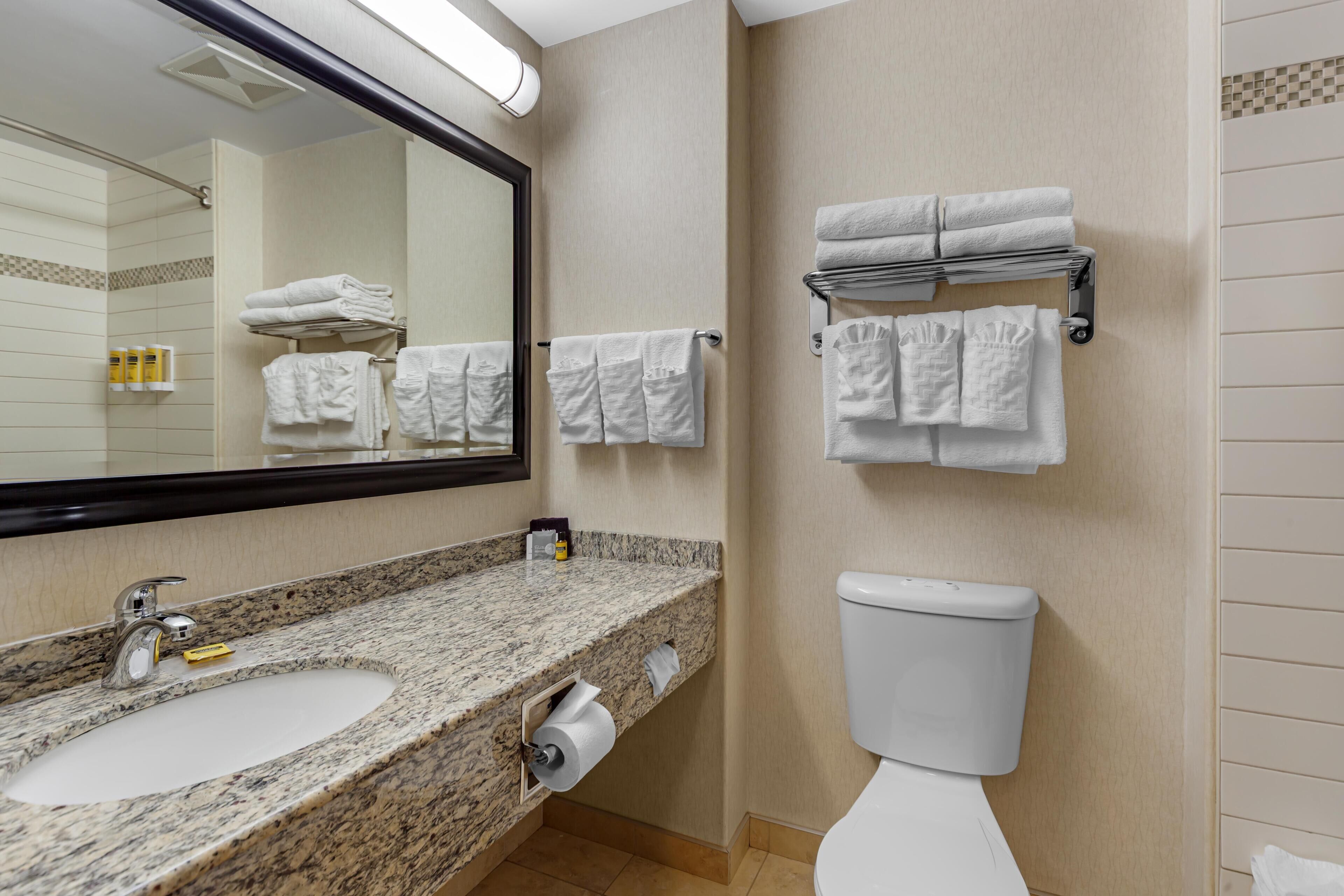 A bathroom with a granite sink, a toilet, and towels on racks.