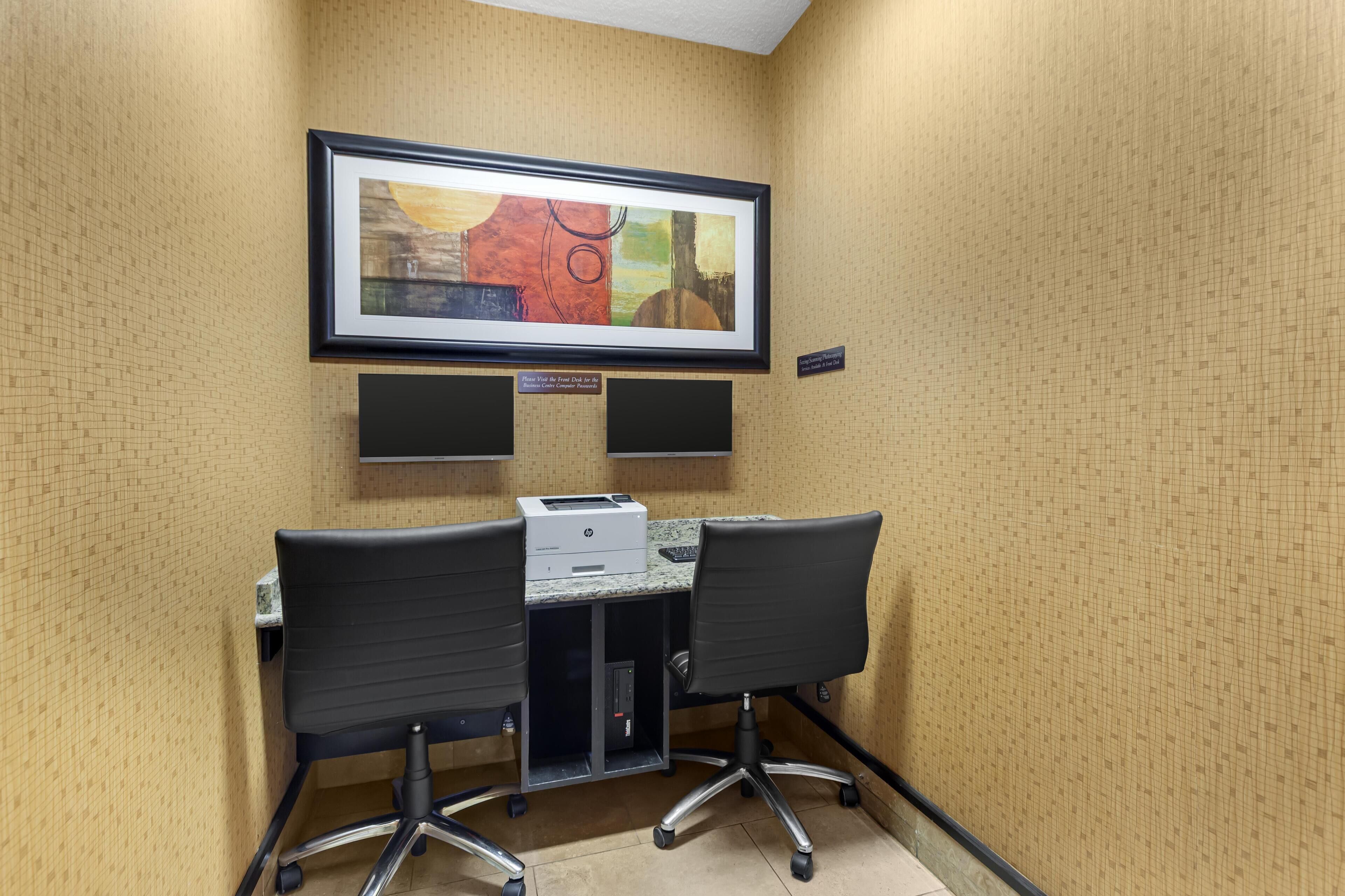 A conference room with a framed abstract painting, two black office chairs, a printer, and a small cabinet.