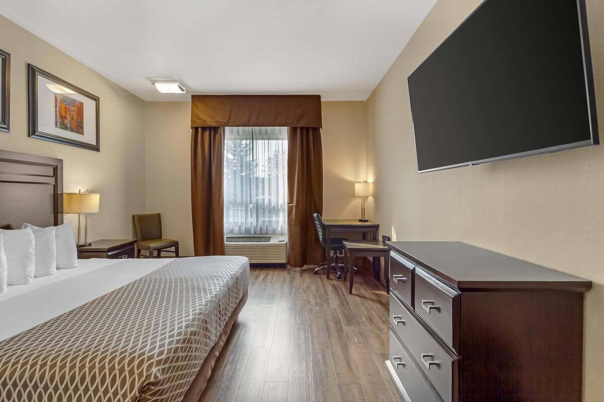 A hotel room with a bed, desk, chair, dresser, and a TV on the wall.
