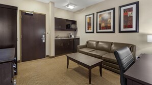 Ein Hotelzimmer mit braunem Ledersofa, einem kleinen Tisch, einer Mikrowelle und einer Küchenzeile. An der Wand befinden sich gerahmte Bilder.