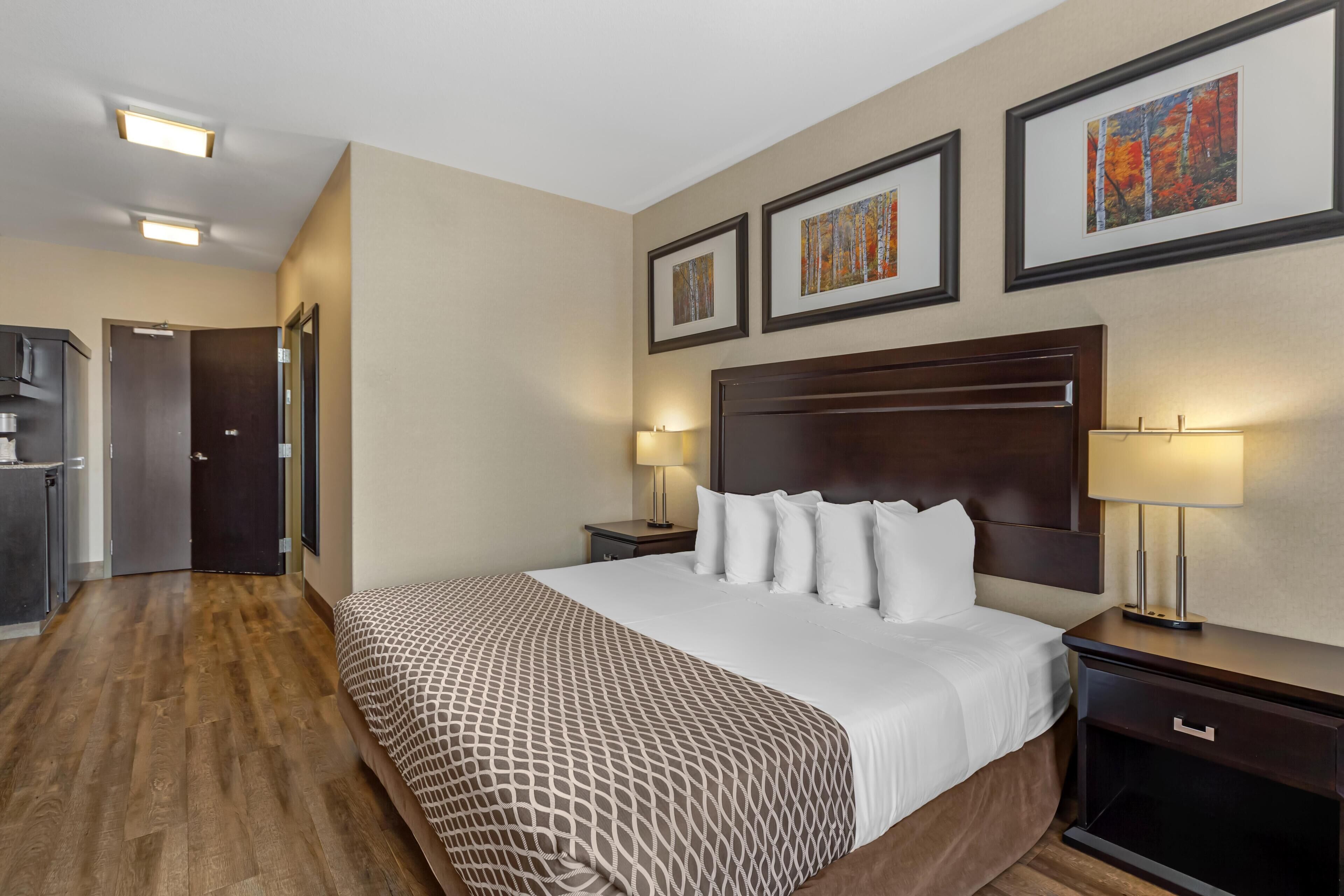 A hotel room with a large bed, a wooden floor, a dark headboard, and framed artwork on the wall.