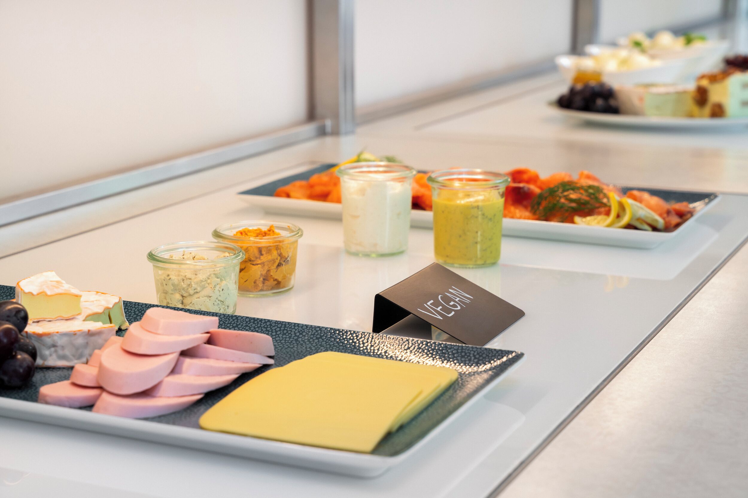 Un bufé con diversos alimentos, incluyendo queso, jamón y opciones veganas.