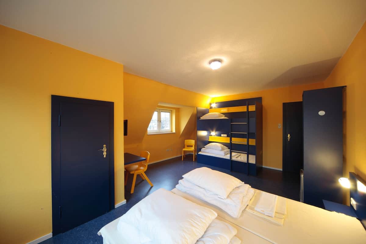 A hotel room with a bunk bed, a desk, a chair, and a window.