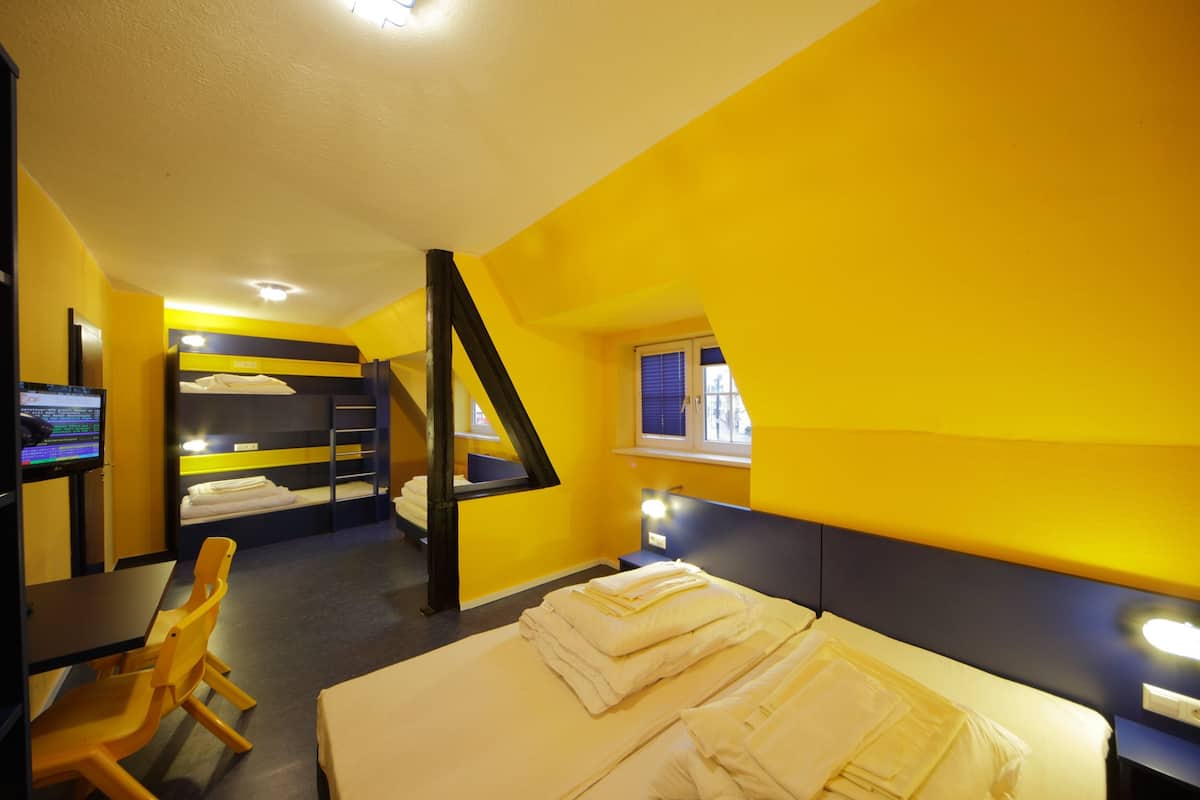 A hotel room with a bed, a desk, a chair, a TV, and a window.