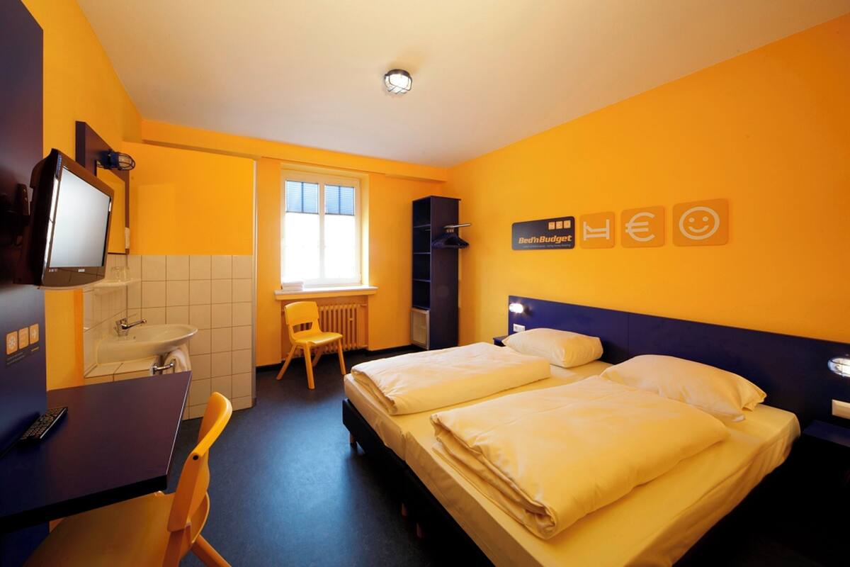 A hotel room with two beds, a desk with a chair, a window, and a television.