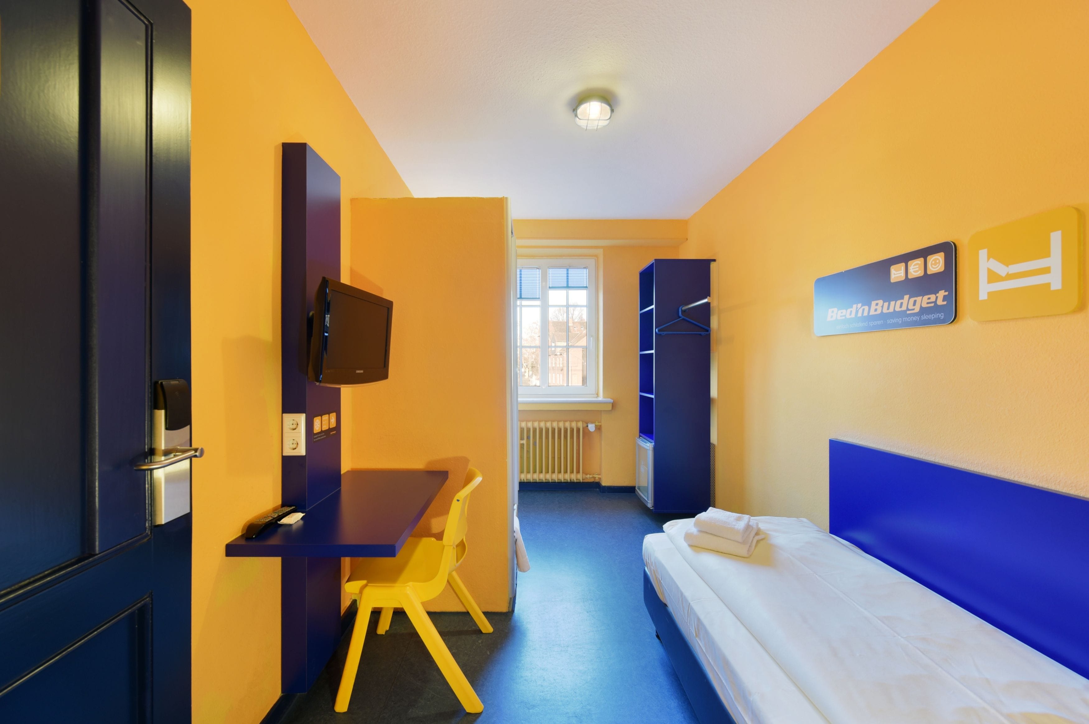 Una habitación de hotel con una cama, un escritorio, una silla, un televisor y un armario.