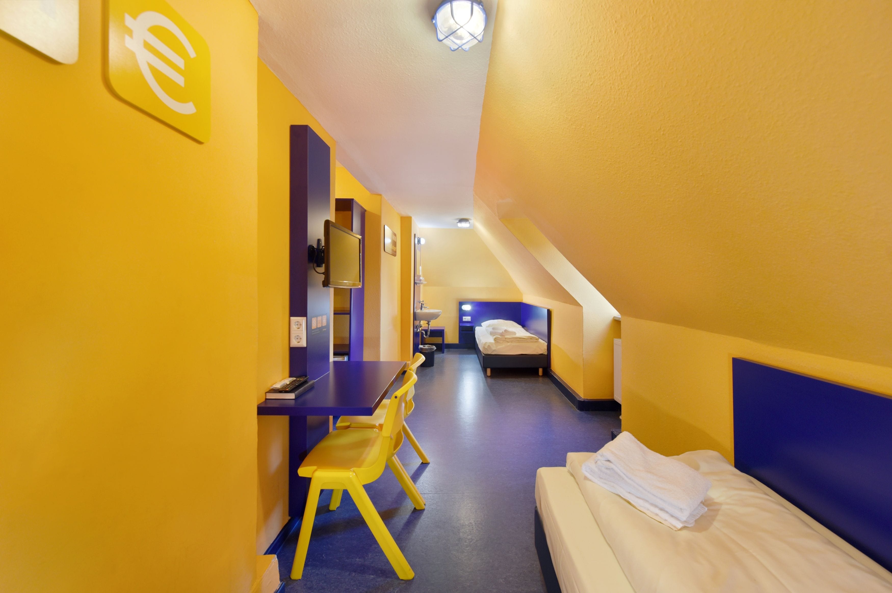 Ein kleines Hotelzimmer mit Bett, Schreibtisch und Stuhl.