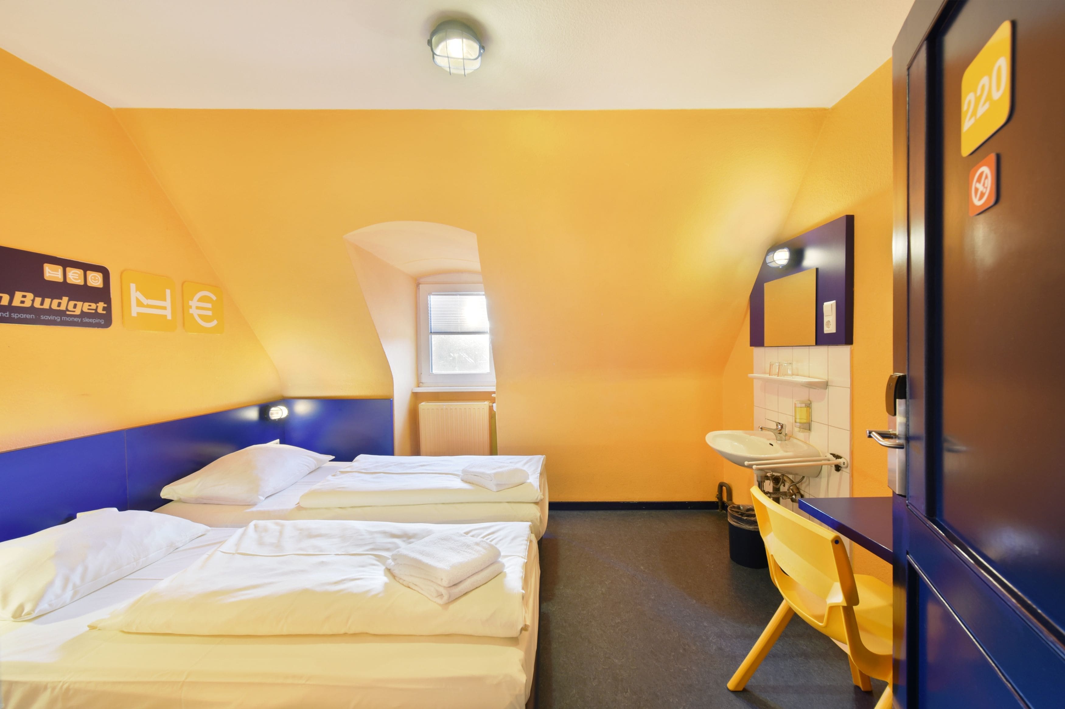 A hotel room with two beds, a bathroom, and a view of the outside.