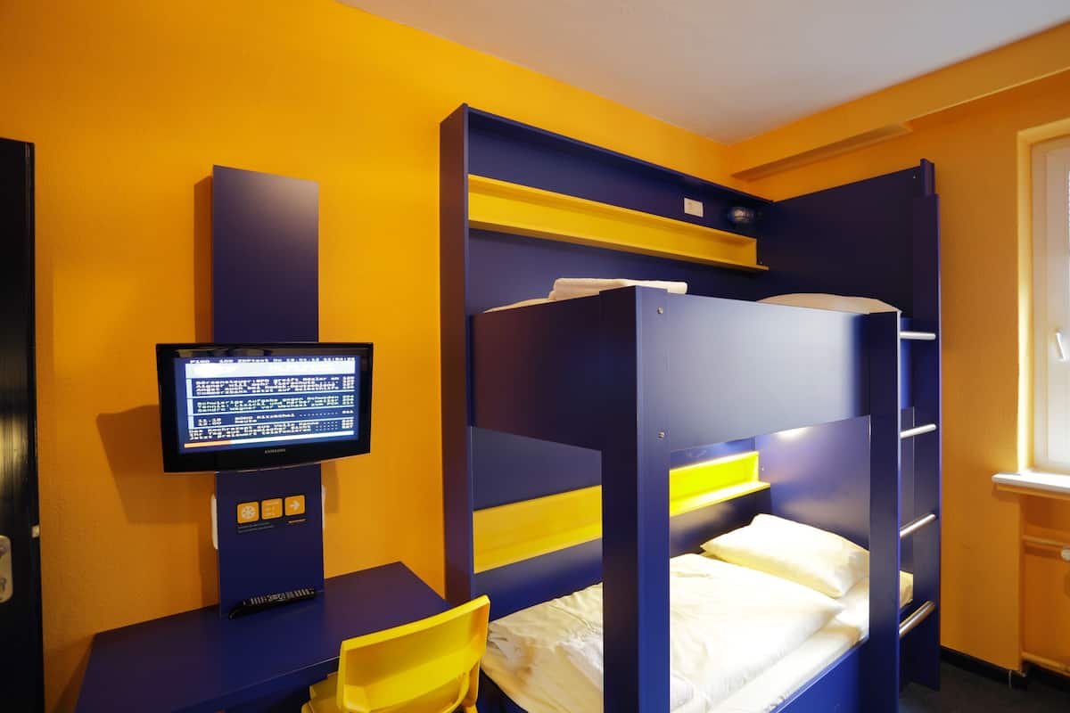 A bunk bed room with a television on a stand, a desk, and a chair.