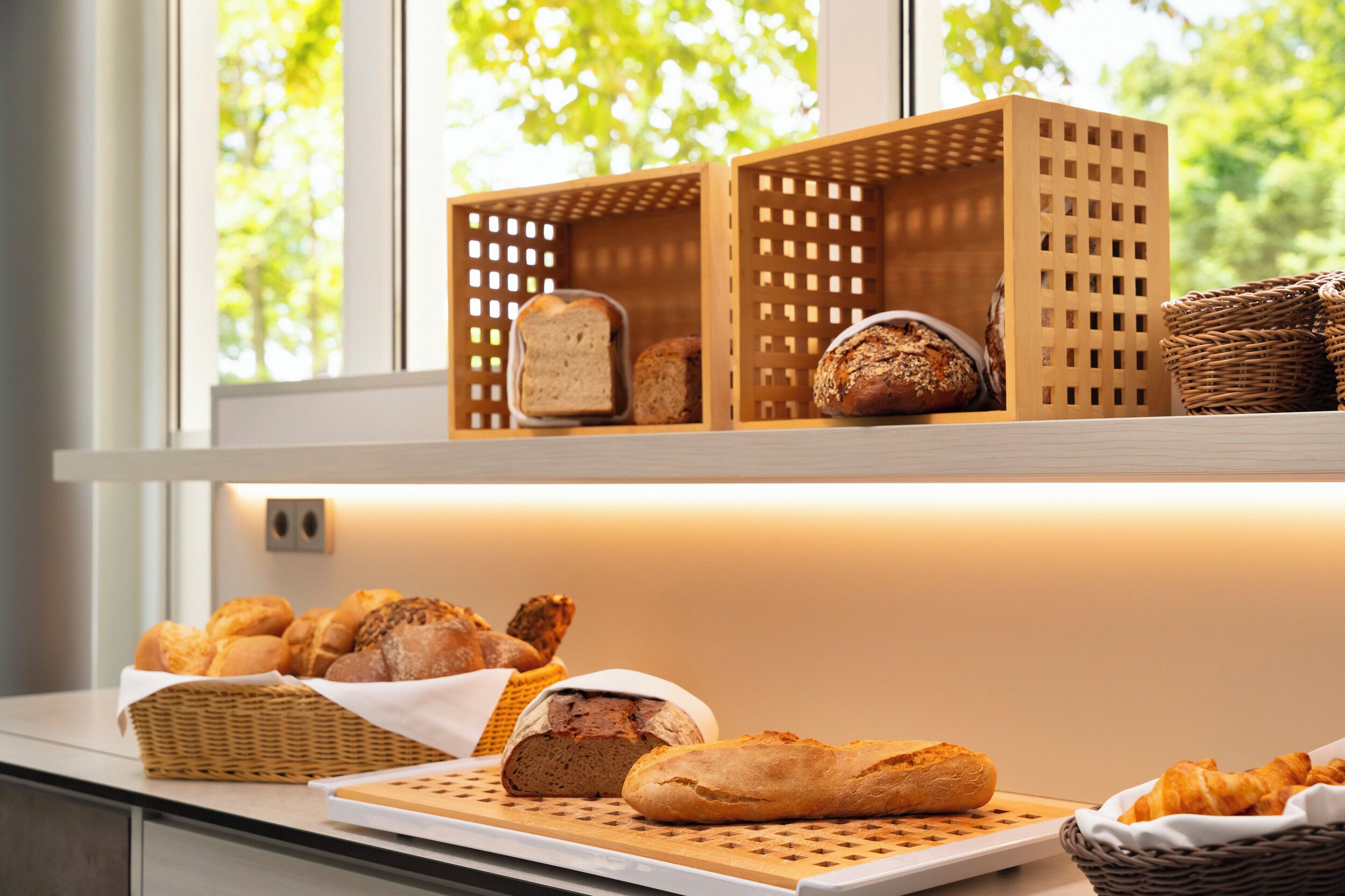 A bakery display with various breads and pastries on a counter near a window with a view of trees.
