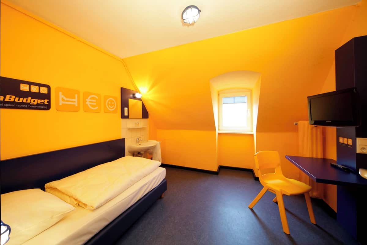 A hotel room with a bed, a desk, a chair, a television, a window, and a bathroom.