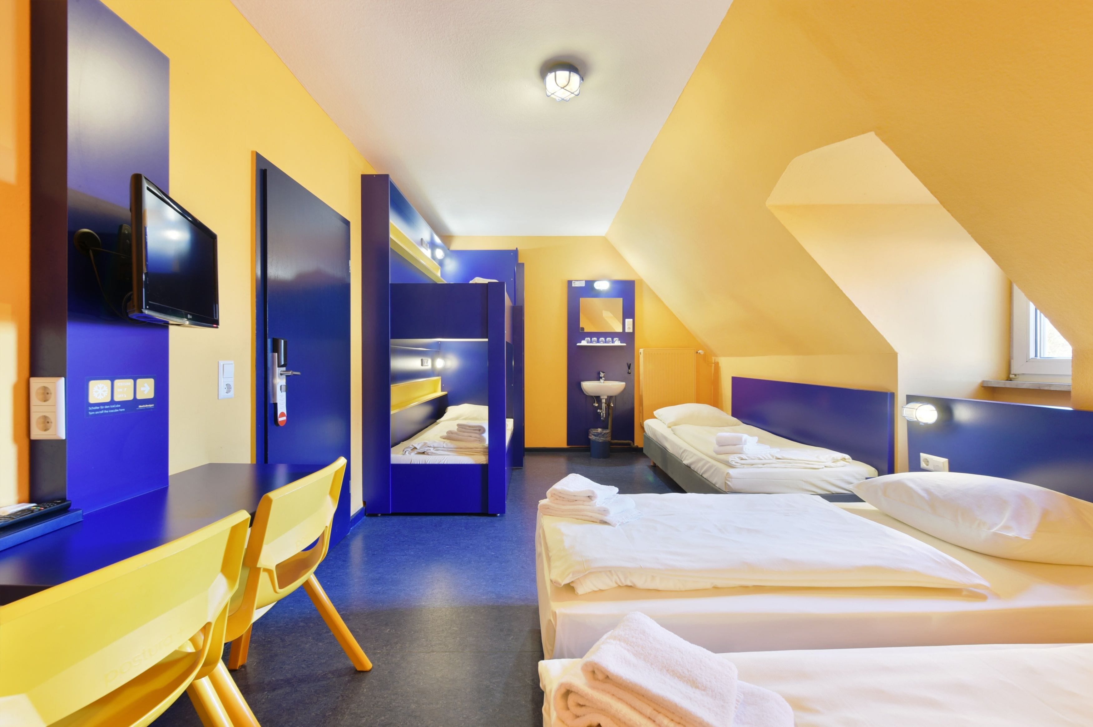 A hotel room with a desk, two beds, a TV, and a bathroom.