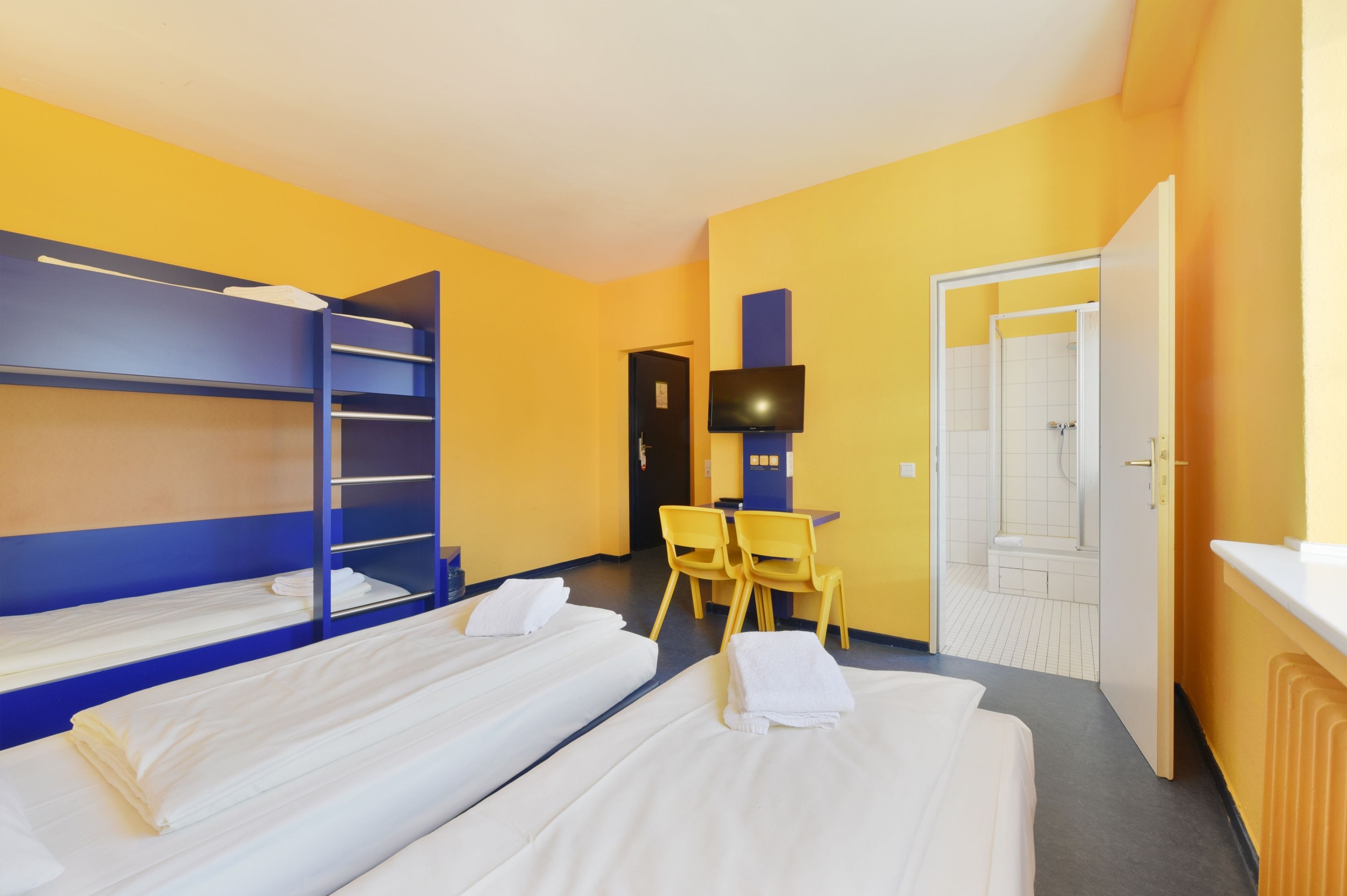 A hotel room with bunk beds, a desk, a chair, a television, and a shower area.