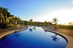 A swimming pool with lounge chairs and palm trees, surrounded by hotel buildings.