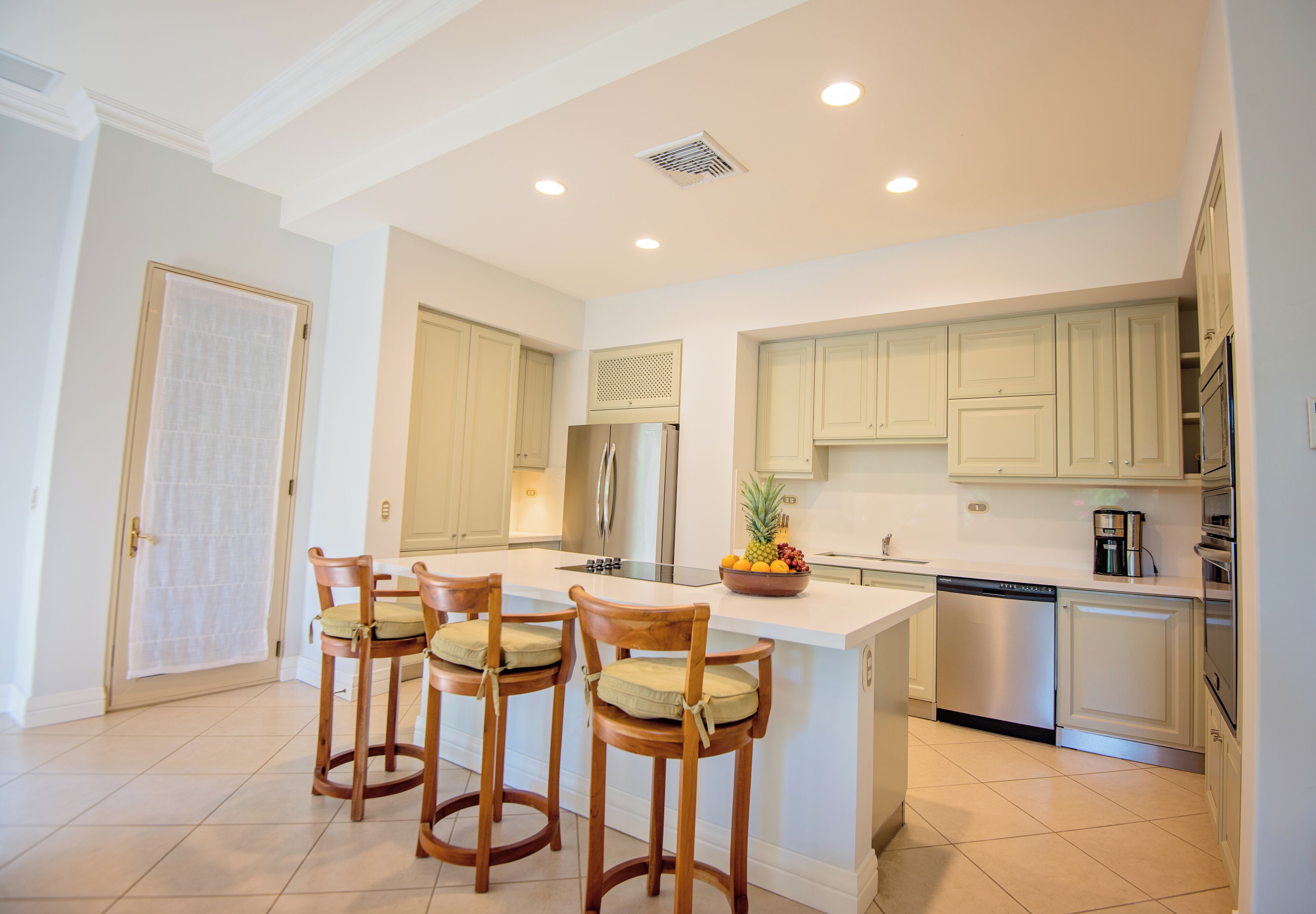 A modern kitchen with a central island, bar stools, stainless steel appliances, and light-colored cabinetry.