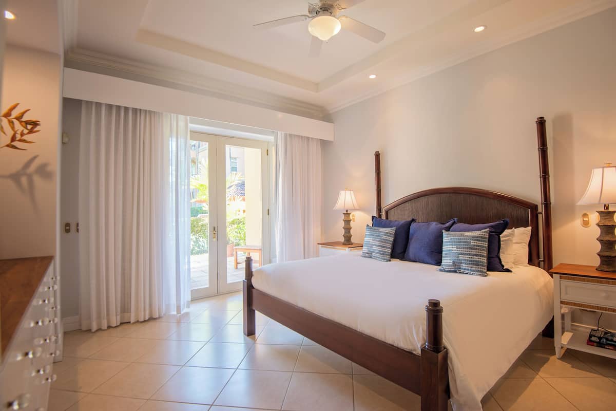 Une chambre spacieuse avec un grand lit, un ventilateur de plafond et une vue sur l’extérieur grâce aux portes vitrées.