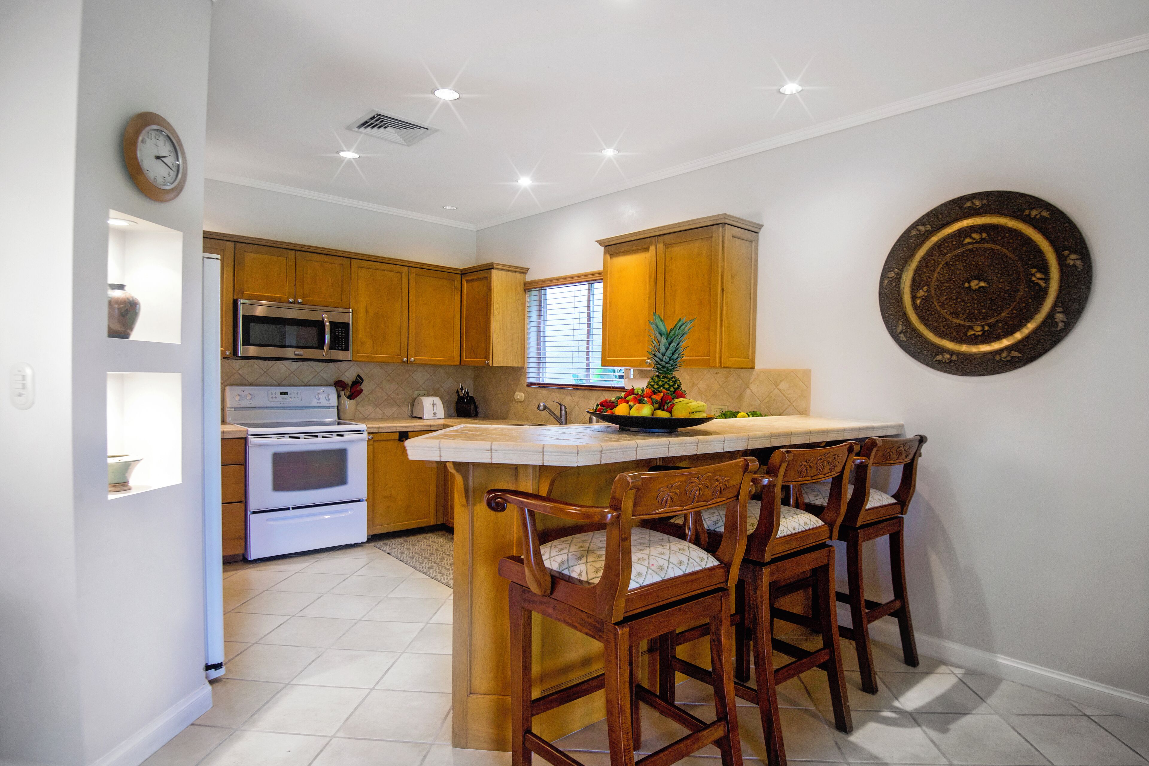 A kitchen with wooden cabinets, a microwave, an oven, and a fruit bowl on the island.