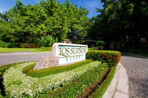 A sign for Los Suenos Resort surrounded by well-maintained gardens and a cobblestone path.