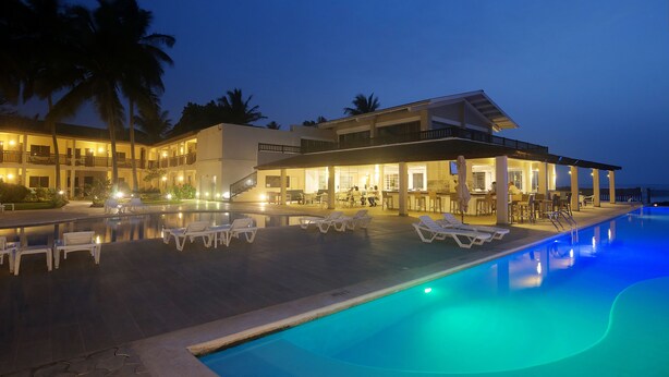 A resort with a swimming pool, lounge chairs, and a covered area with tables and chairs.