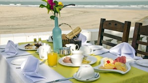 A breakfast table set on a balcony overlooking a beach with a view of the ocean.