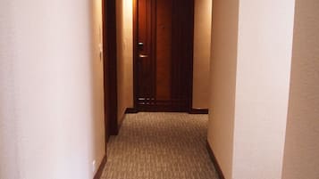 Ein schmaler Korridor mit Teppichboden, einer Holztür am Ende und Einbauleuchten in der Decke.