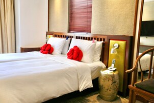 Una habitación de hotel con una cama doble, dos almohadas, una mesita de noche con lámpara y una silla.