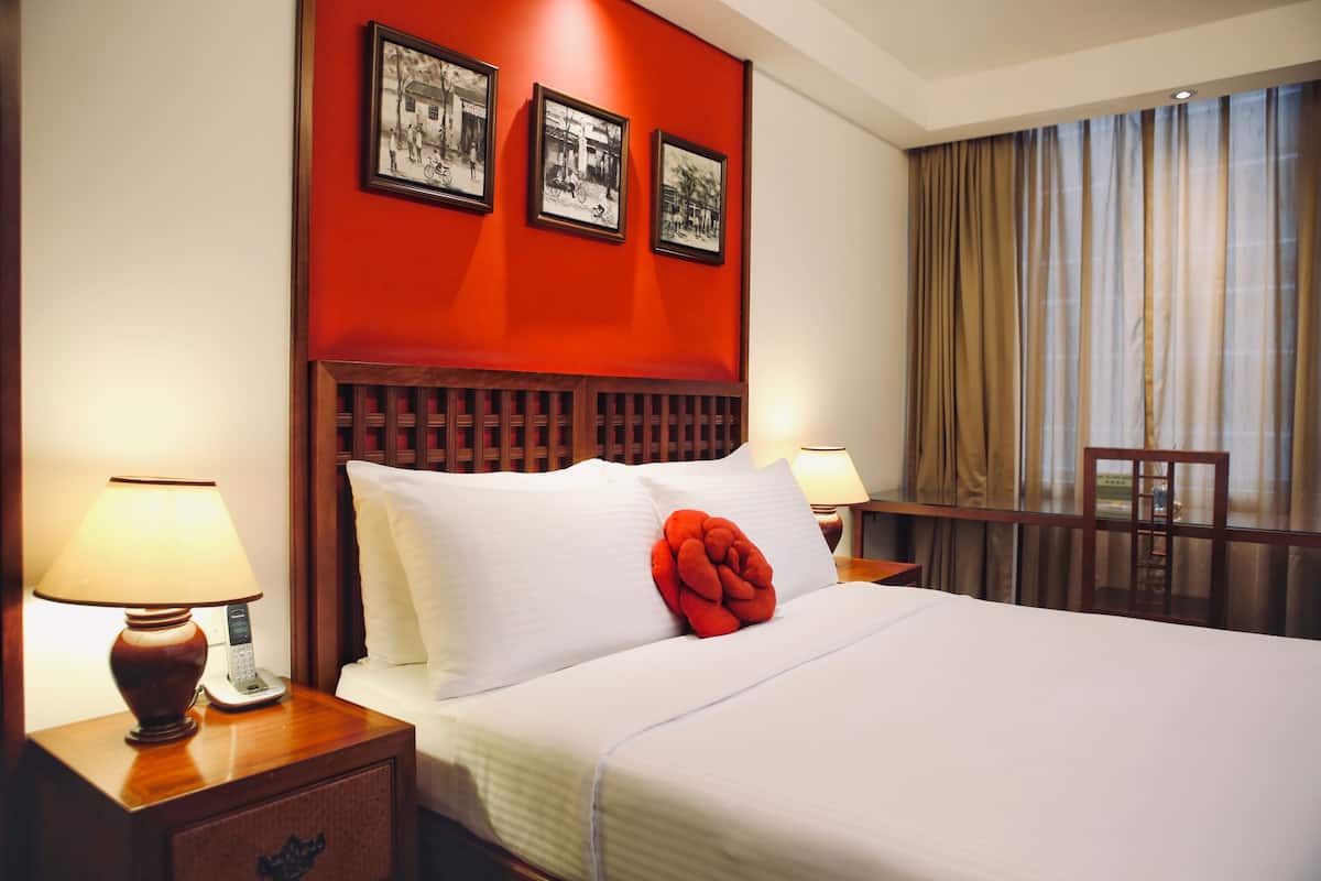 A hotel room with a large bed, a wooden headboard, a nightstand with a lamp, and a chair.