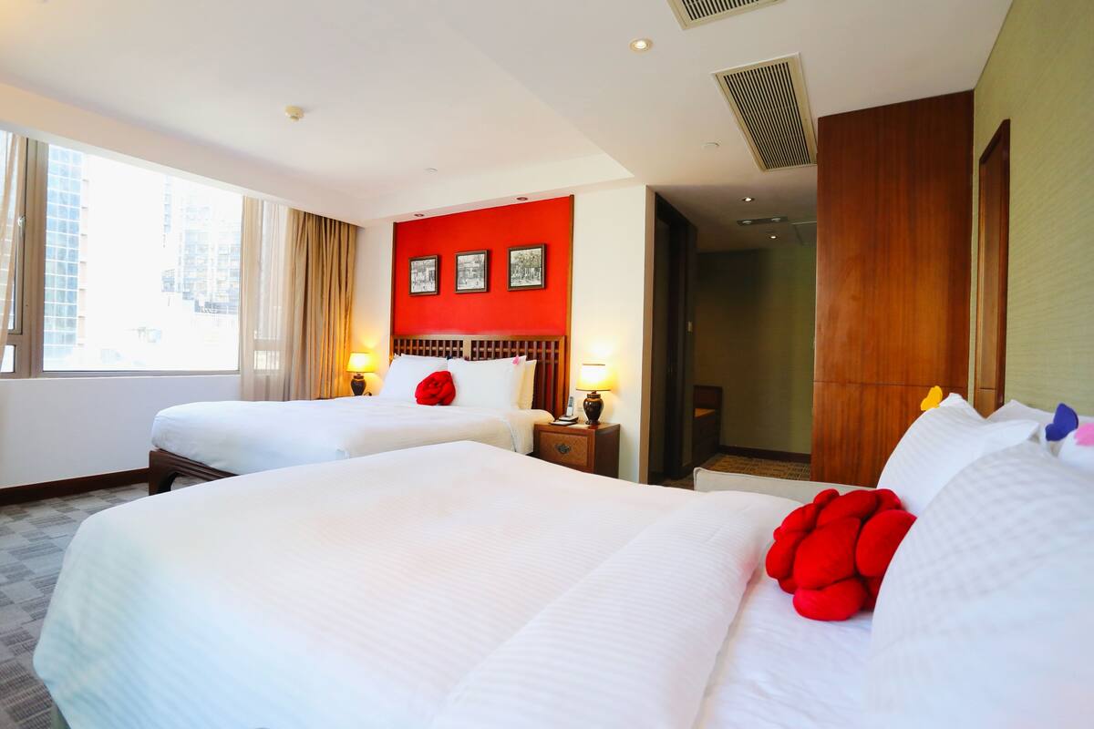 A hotel room with two beds, a red accent wall, and a large window.