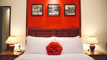 A hotel room with a red accent wall, a large bed with white linens, a red decorative pillow, and three framed pictures above the bed.