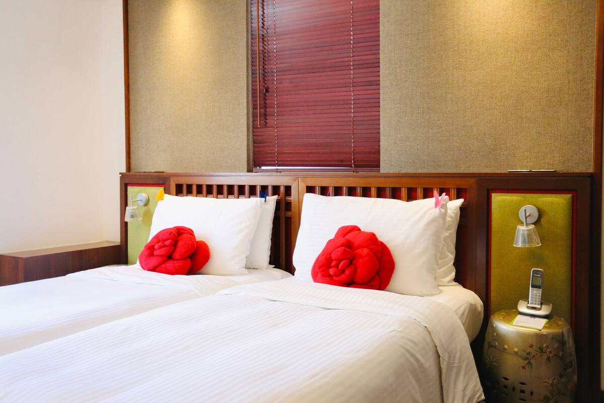 A double bed with white bedding and two red decorative pillows, a bedside table with a lamp, and a telephone.