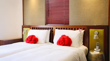 A double bed with white bedding and two red decorative pillows, a bedside table with a lamp, and a telephone.
