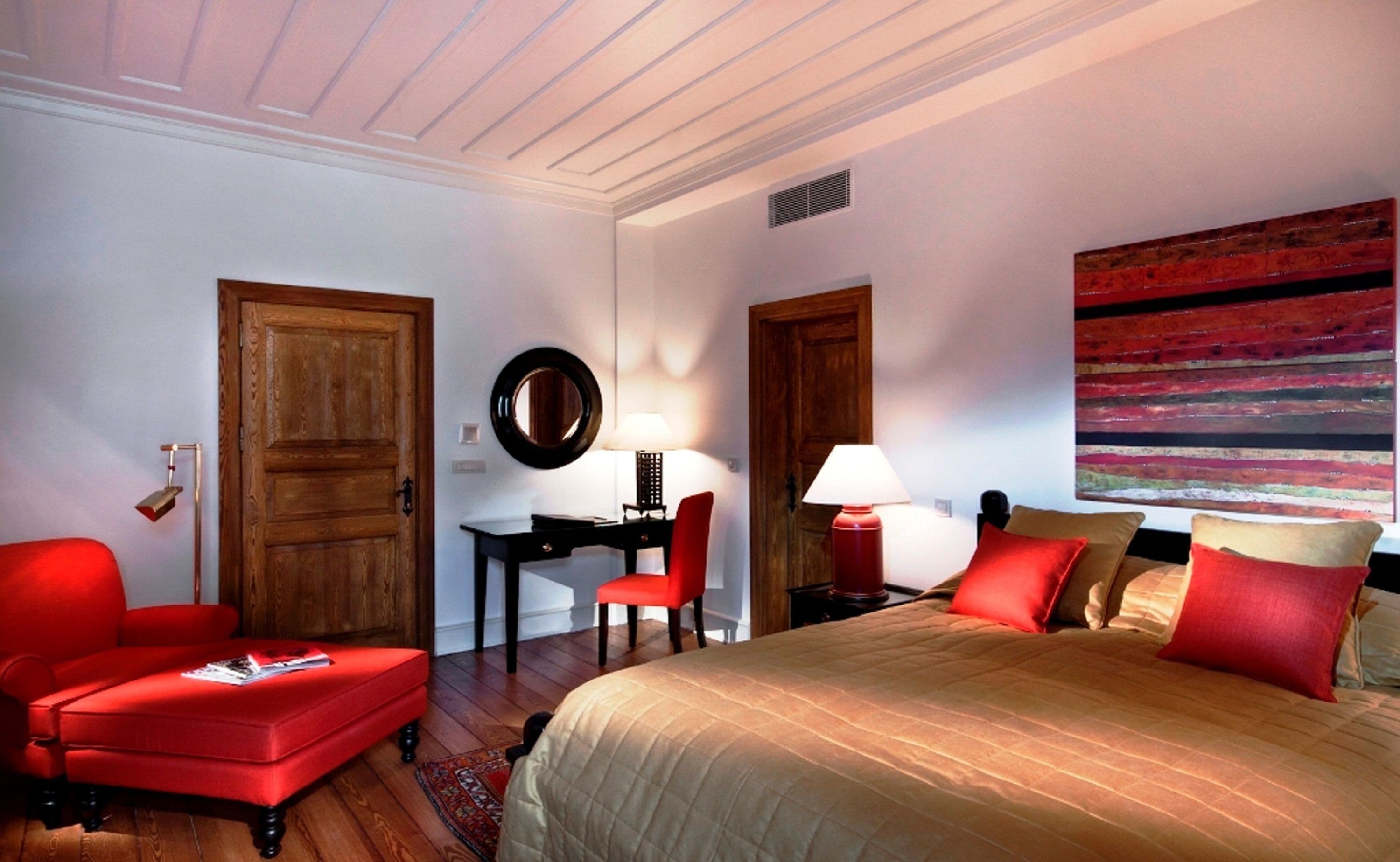 Una habitación de hotel con cama, escritorio, silla y un sillón rojo.