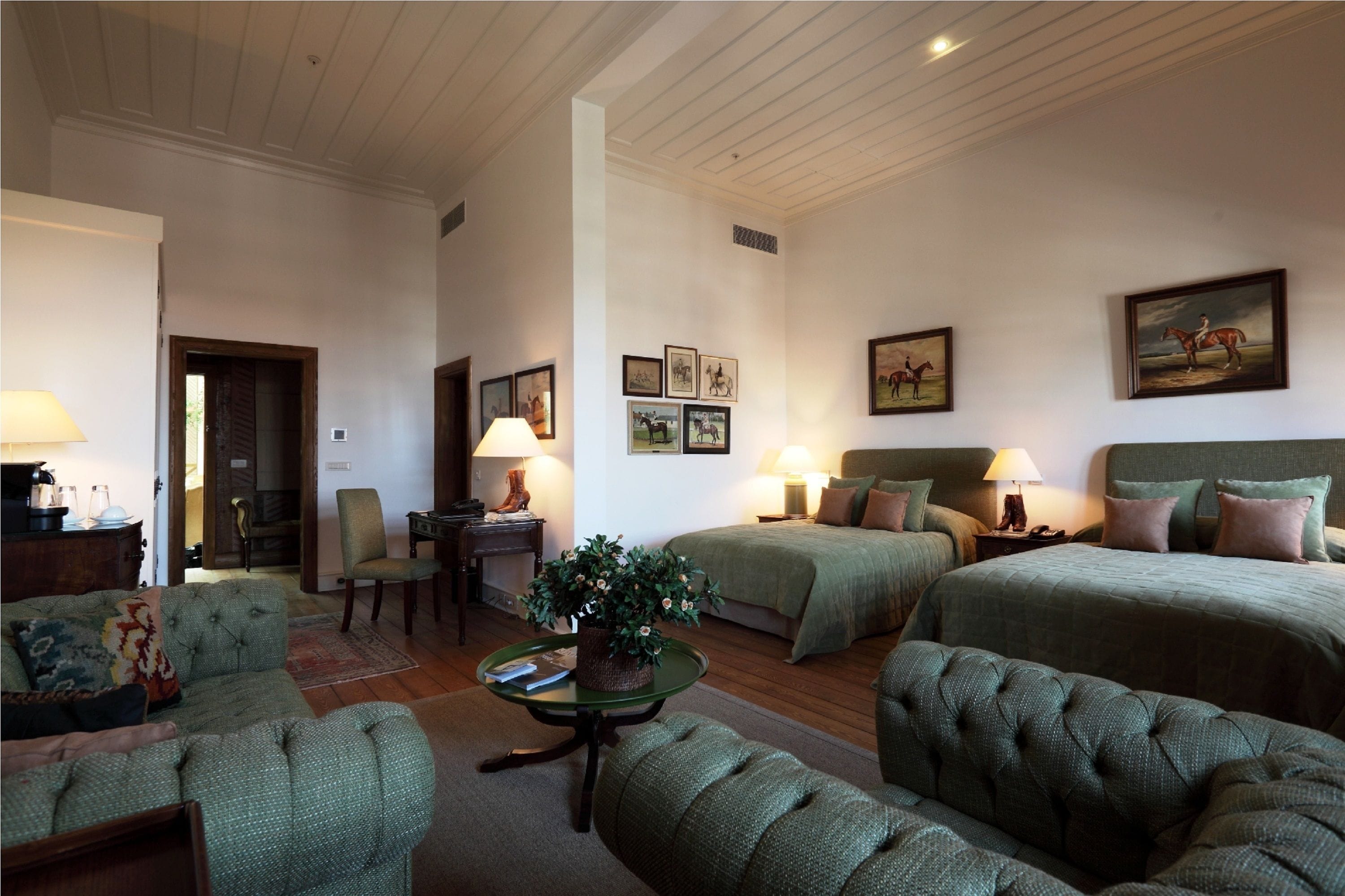 A room with two beds, a sofa, a table with a plant, and framed pictures on the wall.