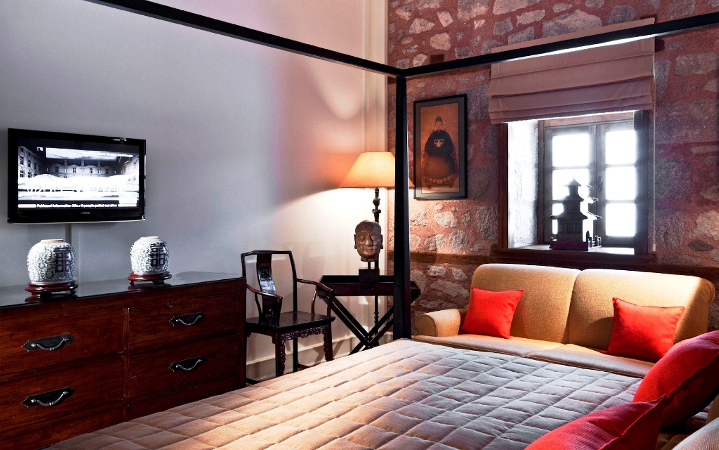 A bedroom with a bed, a dresser, a television, a lamp, and a window with a view of a pagoda.