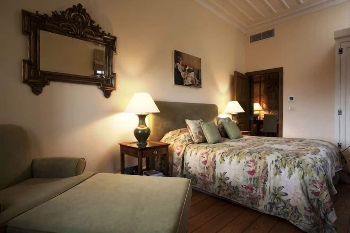 Ein Schlafzimmer mit einem Bett, zwei Nachttischen mit Lampen, einem Sessel, einem Spiegel und einem Bild an der Wand.