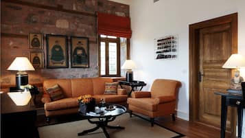 A cozy living room with a stone wall, a wooden door, and a fireplace. There are two sofas, a coffee table, and a side table with lamps.