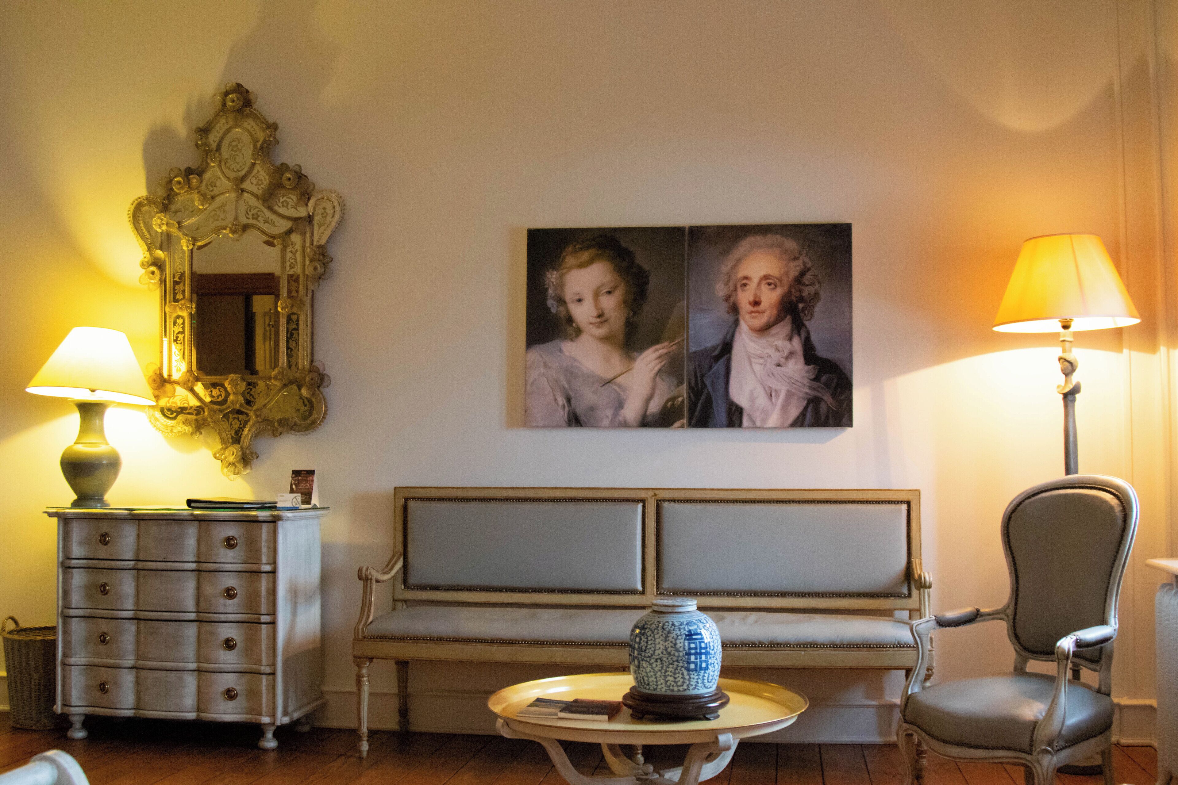 A room with a sofa, a chair, a table with a vase, a lamp, a dresser, and a mirror.