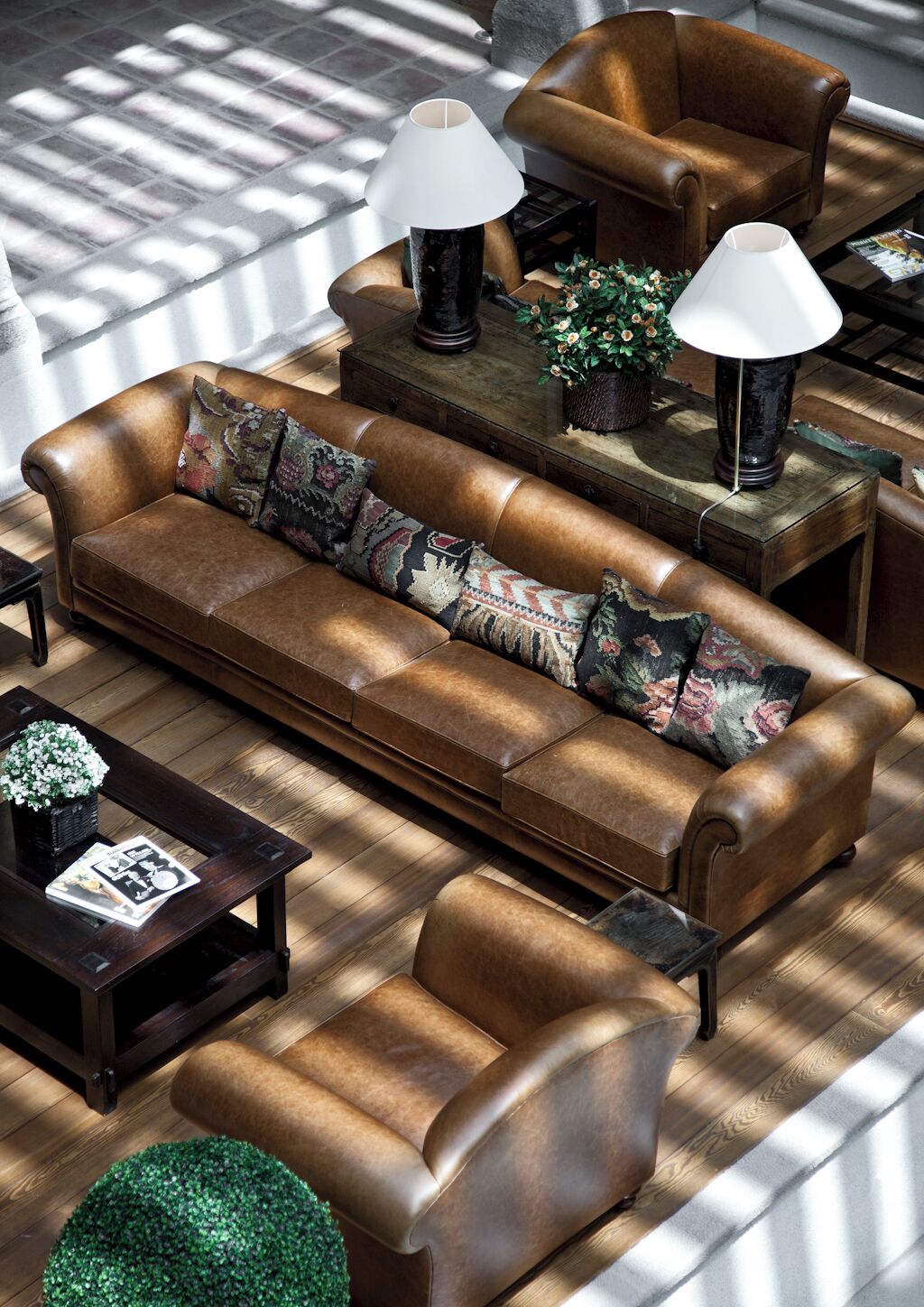 A modern living room with a leather sofa, armchairs, and a coffee table. There are two lamps on side tables and a potted plant.
