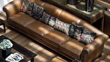 A modern living room with a leather sofa, armchairs, and a coffee table. There are two lamps on side tables and a potted plant.