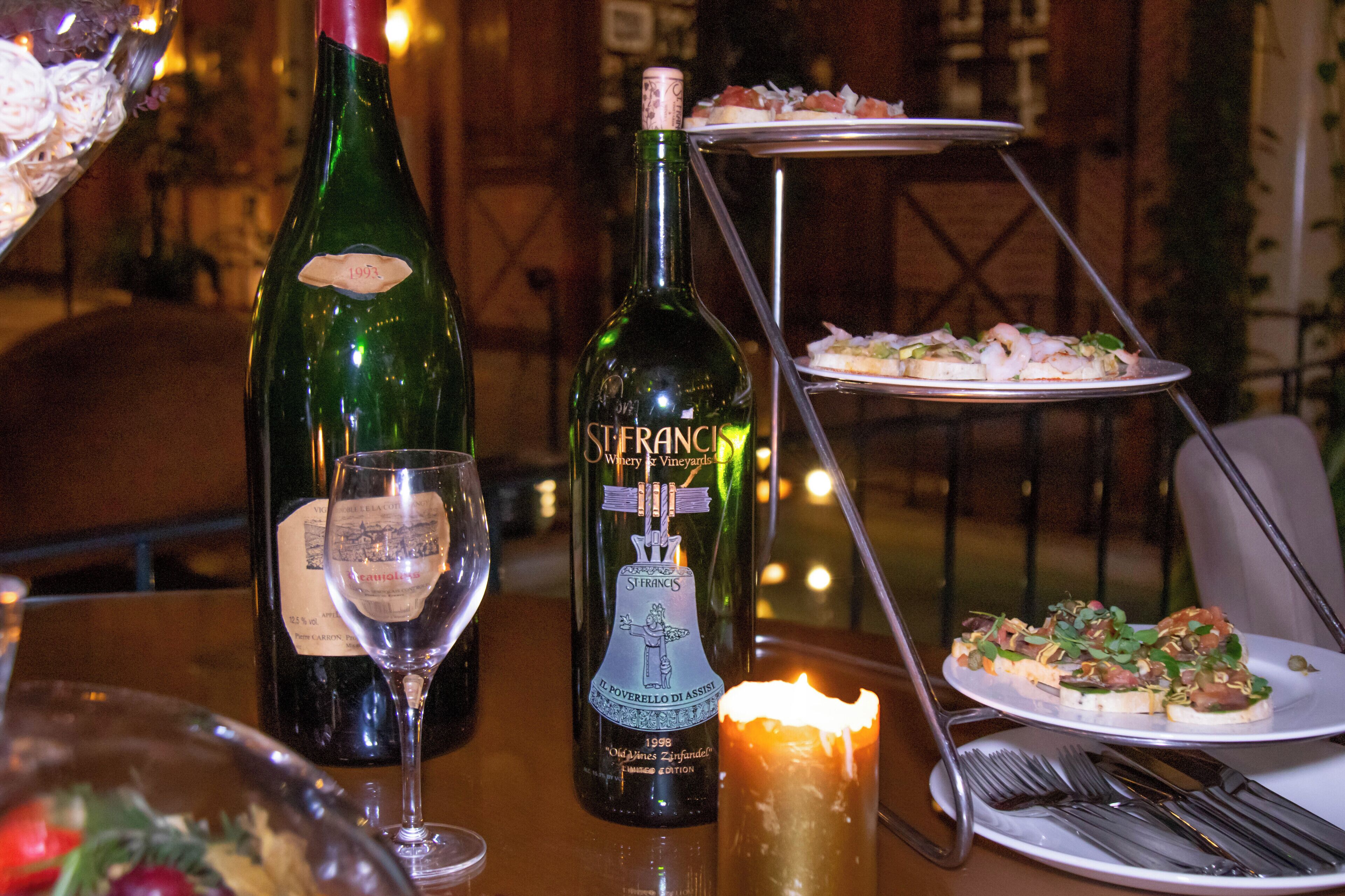 A table with a bottle of wine, a glass, a candle, and a plate of food.