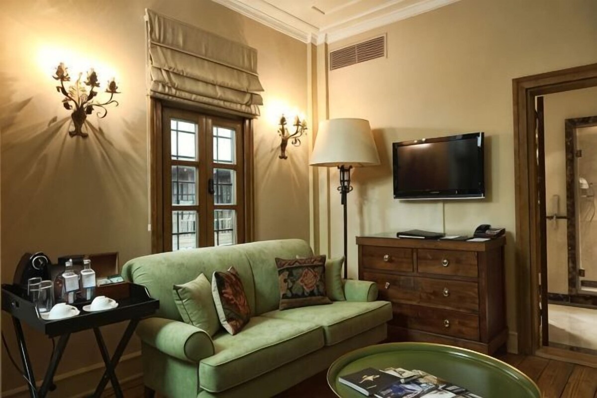 A living room with a green sofa, a television, a lamp, and a window with curtains.