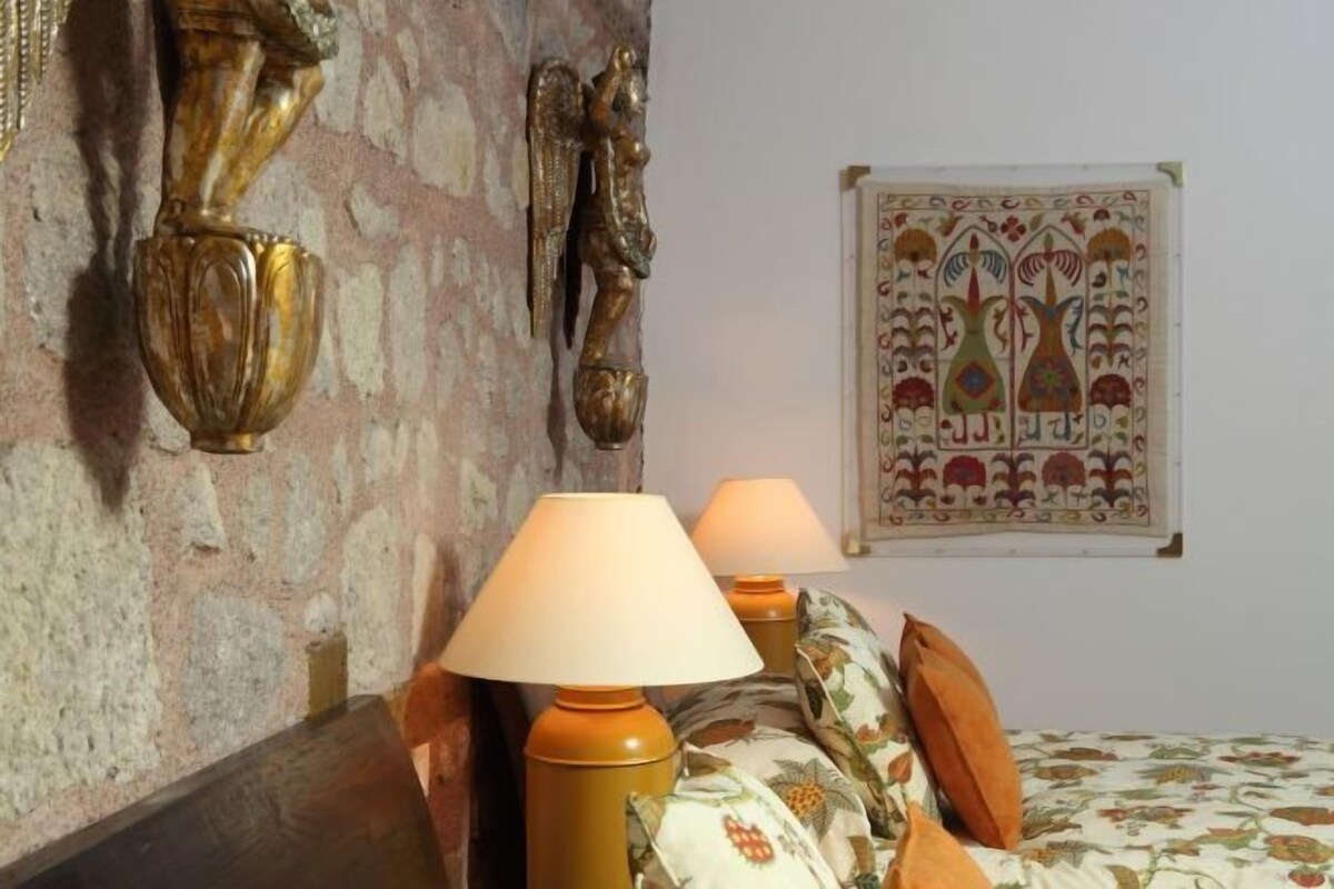 A room with a bed, two wall-mounted lamps, a decorative wall piece, and a patterned bedspread.
