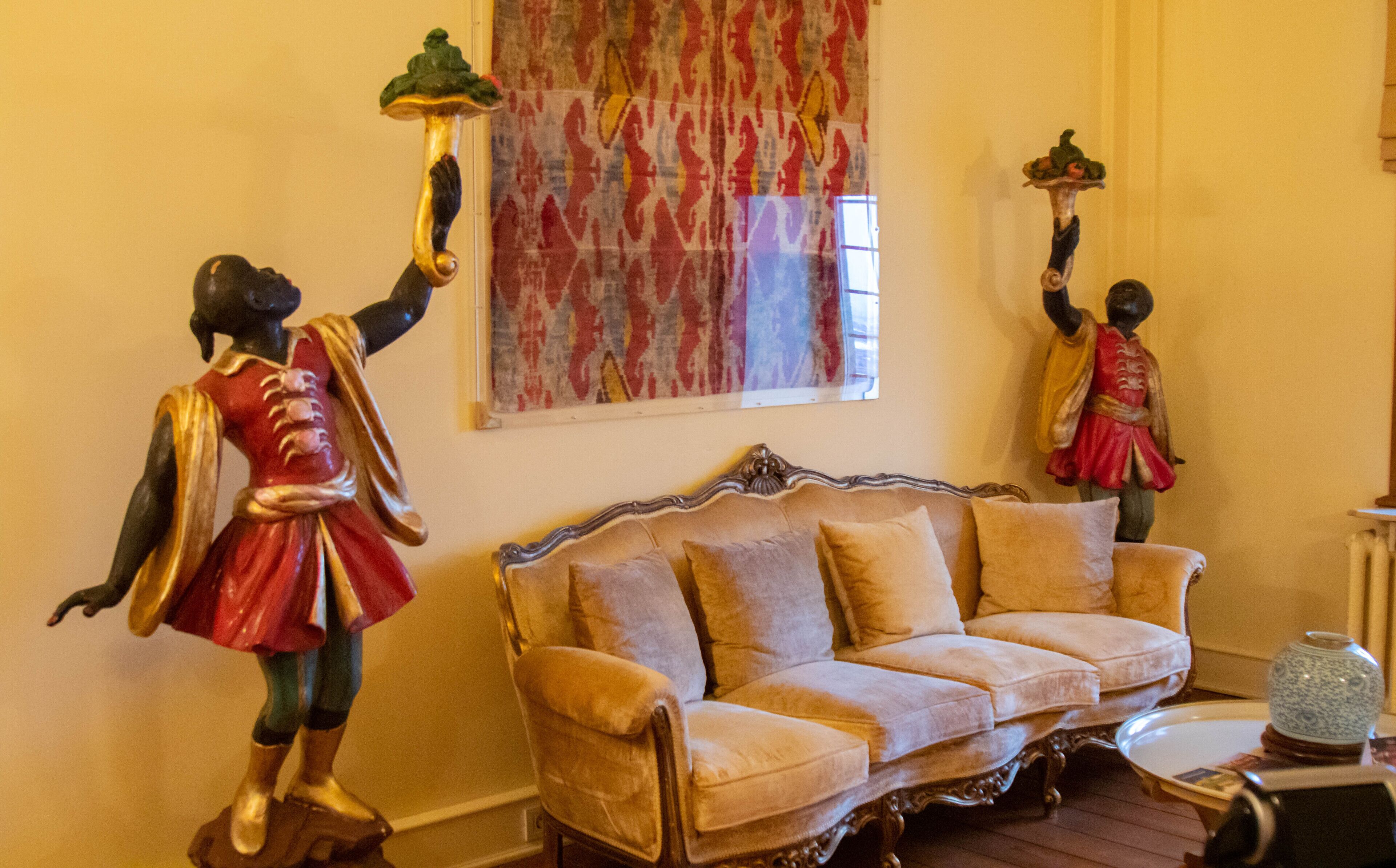 A room with a vintage sofa, two wall-mounted statues, and a patterned curtain.
